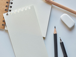 Flat lay of a spiral notebook, pencils, pen, and eraser on a white background.
