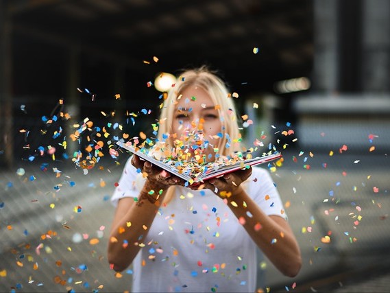 Woman blowing confetti from a book. 